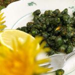 Ett fat med stekta maskrosknoppar, med ett par maskrosblommor i förgrunden.
